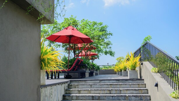 Un escalier menant à un espace sur le toit, aménagé avec des sièges extérieurs et des parasols rouges.