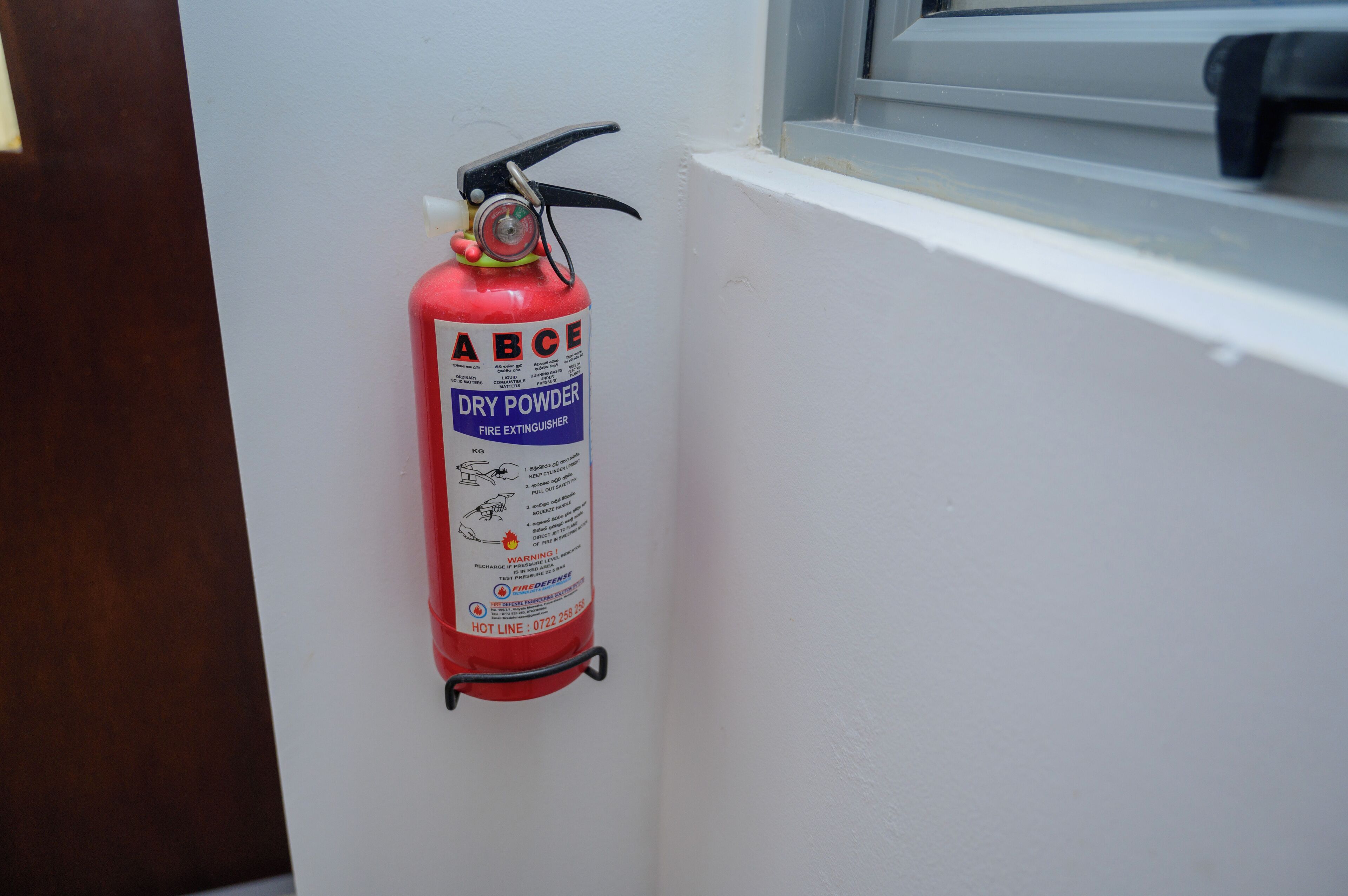 Een brandblusser bevestigd aan een witte muur in de buurt van een raam.