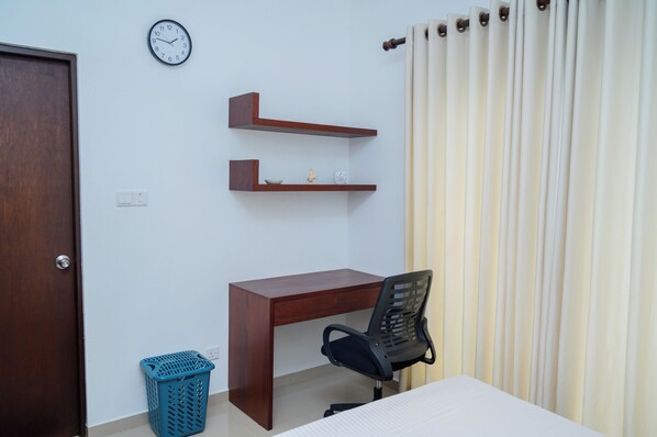 A bedroom with a wooden desk, a chair, a clock, and a curtain.