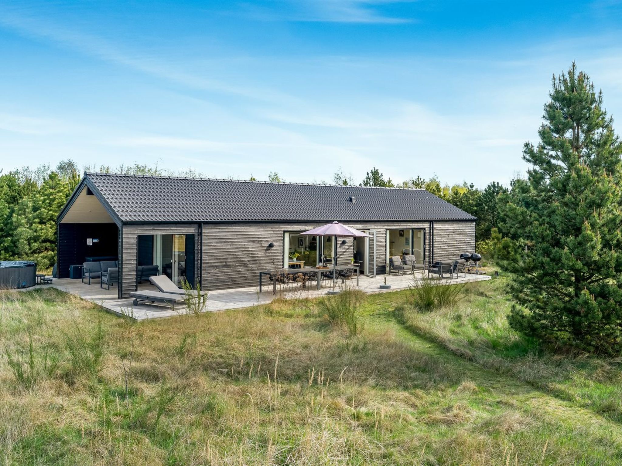 Et moderne hus med en stor terrasse, udendørs møbler og en overdækket sektion.