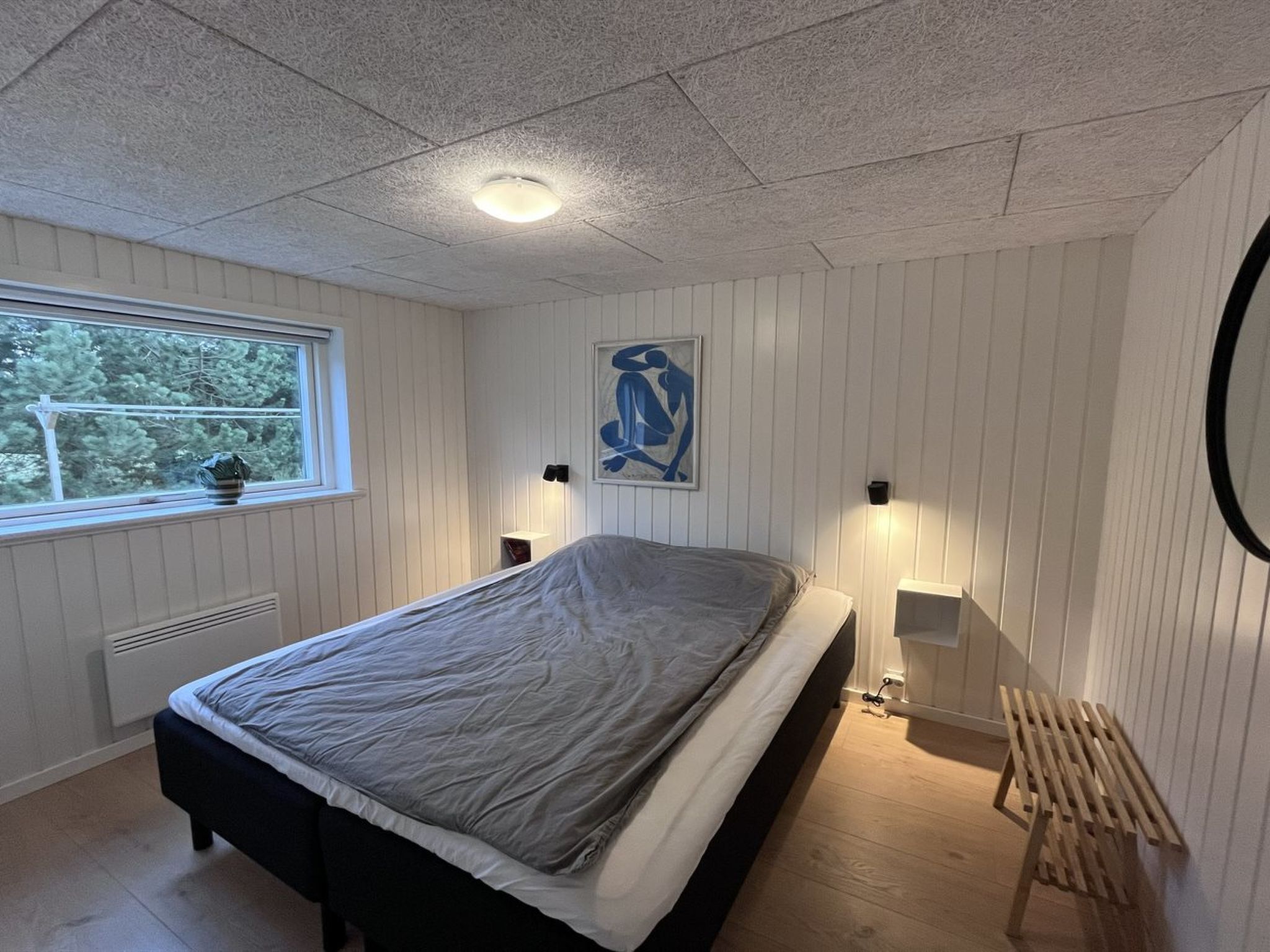 Een slaapkamer met een bed, een raam, een wanddecoratie en een nachtkastje.