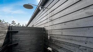 Eine Holzterrasse mit einem Metalltor, einer Metallduschbrause und einer Metallleitung an der Wand.