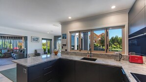 Een moderne keuken met donkere kastjes, een groot eiland en een raam met uitzicht op een woonwijk.