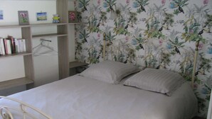 A bedroom with a bed, a metal headboard, a shelf with books, and a floral wallpaper. - Gîte 10 minutes from the beach (Hudimesnil)