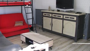 A compact room with a bunk bed, a red sofa, a small table, a cabinet with a TV, and a chair. - Gîte 10 minutes from the beach (Hudimesnil)