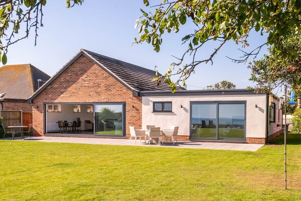 A modern house with a brick exterior, large sliding glass doors, and a patio with outdoor furniture.