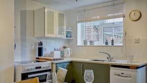 A modern kitchen with white cabinets, a built-in oven, a sink, and a window with a view of the outside. - Rose Cottage | Dog-Friendly Village Stay, 2 Minutes from the Beach (Winterton-on-Sea)