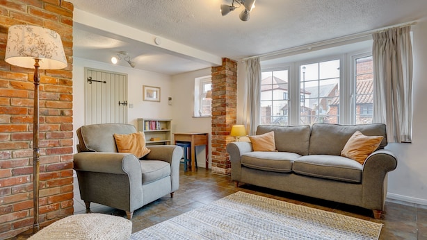 A cozy living room with a brick wall, two sofas, a floor lamp, and a bookshelf. - Rose Cottage | Dog-Friendly Village Stay, 2 Minutes from the Beach (Winterton-on-Sea)