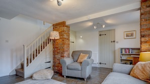 A living room with a staircase, a brick fireplace, and a bookshelf. - Rose Cottage | Dog-Friendly Village Stay, 2 Minutes from the Beach (Winterton-on-Sea)
