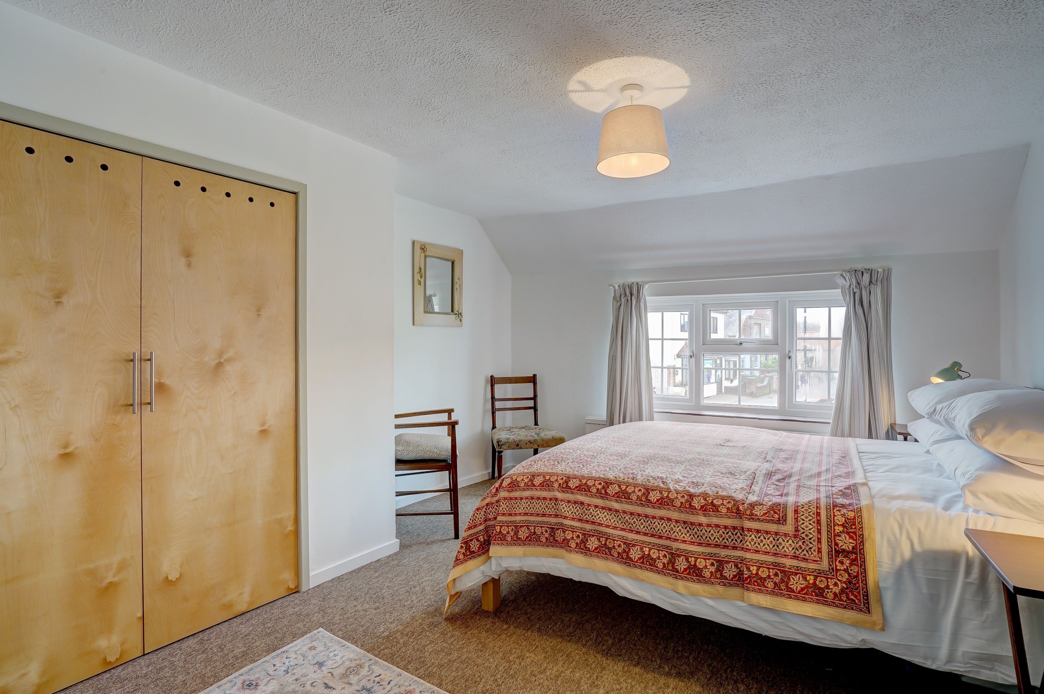 A bedroom with a large bed, a wardrobe, a chair, a window with curtains, and a ceiling light.