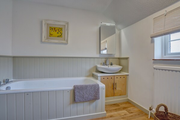 Een badkamer met een bad, een wastafel, houten kastjes, een spiegel en een foto in een lijst aan de muur.