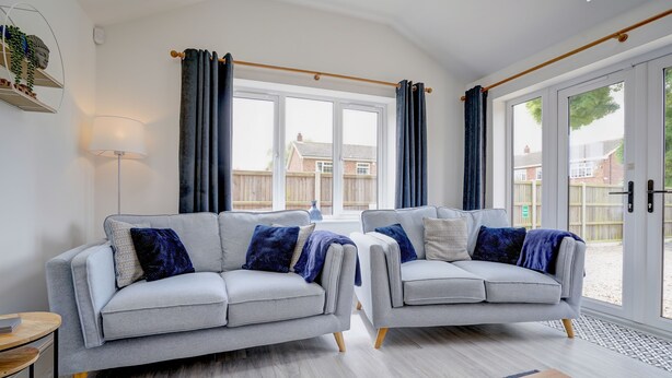 A modern living room with two grey sofas, a floor lamp, and a large window with curtains.