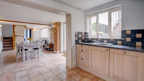 A modern kitchen with a large window, a dining area with a table set for four, and a staircase leading to another room.