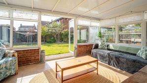 A conservatory with a wooden table, a sofa, and a view of the garden. - Sanderlings | Dog Friendly Family House, 5 Mins to Winterton Beach (Winterton-on-Sea)