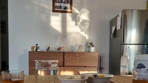 Una mesa de comedor con platos, vasos y tazones, un refrigerador y un armario de madera con objetos decorativos.