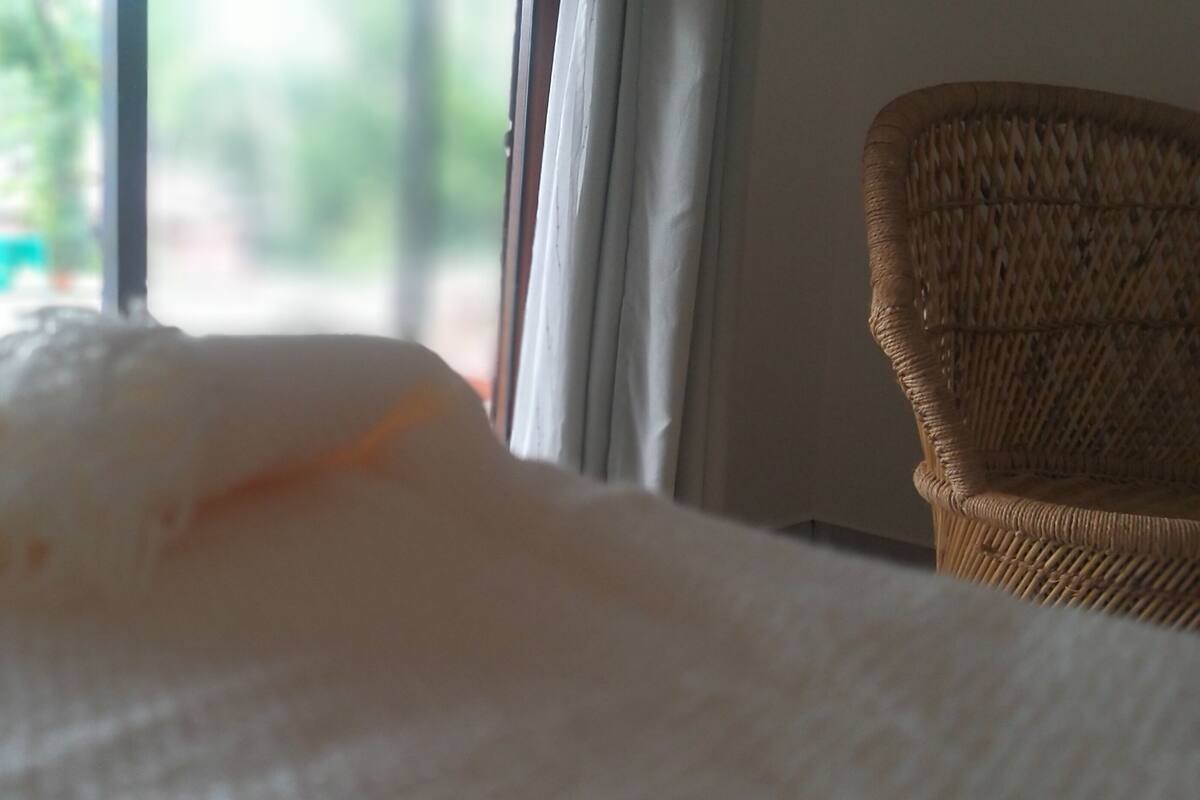 A bed with a white blanket, a wicker chair, and a window with curtains.