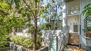 Un edificio moderno con fachada de vidrio, una escalera que lleva a un nivel superior y un jardín bien cuidado con diversas plantas y árboles.