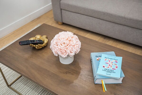 A coffee table with a vase of pink roses, a remote control in a gold holder, and a stack of books titled "The New York Times Hours Los Angeles & Beyond." - Beautiful home in Prime Weho w/Private Rooftop Spa! Incl. Parking/Laundry/Wifi (Los Angeles)