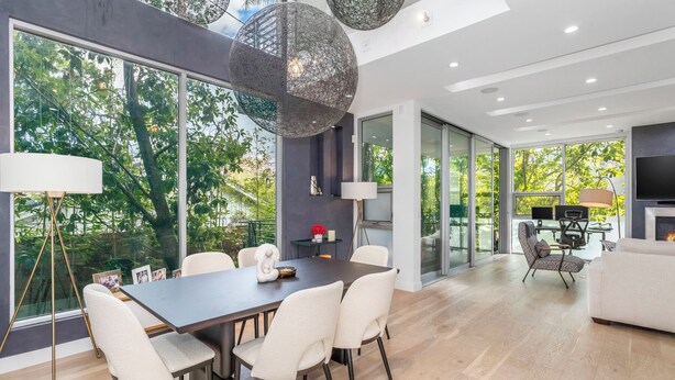 Un comedor moderno con una mesa de madera oscura, sillas blancas y ventanas amplias que ofrecen vistas al verdor.