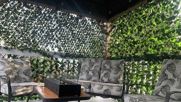An outdoor seating area with a sofa and table, surrounded by a lattice fence and lush greenery.