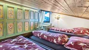 Una habitación con cuatro camas, una mesa, sillas, un ventanal con vistas y cuadros con motivos florales en la pared.