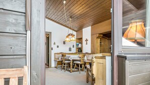 Un interior de madera con una mesa y sillas de comedor, una lámpara colgante y una cruz en la pared.
