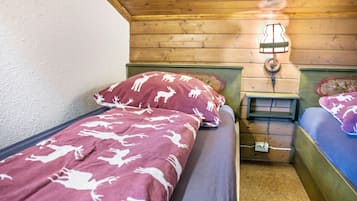 Una habitación pequeña y acogedora con dos camas individuales, techo de madera y una mesita de noche con lámpara.