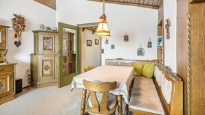 Una habitación con techo de madera, una mesa de comedor con mantel blanco, un banco de madera con cojines y una lámpara colgante.