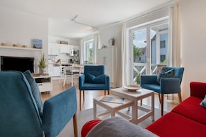 A modern living room with a TV, blue and red sofas, a coffee table, and a kitchen in the background.