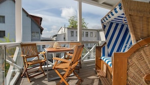 A wooden deck with a table and chairs, a wicker chair, and a view of buildings. - Holiday Apartment 'Inselliebe Rügen' with Balcony, Ahoi Pool & Sauna Included (Sellin)