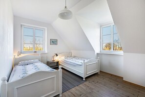 Ett sovrum med två sängar, ett fönster, ett element och en tavla på väggen.