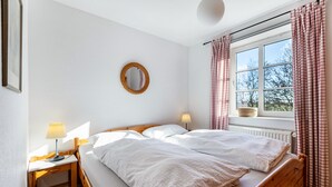 Ein Schlafzimmer mit Bett, Nachttischen, einer Lampe, einem Spiegel und einem Fenster mit Vorhängen.