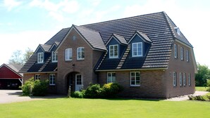 Ein großes, zweistöckiges Haus mit steilem Dach, einer Ziegel-Fassade und einem Hauseingang mit Tür und Fenstern.