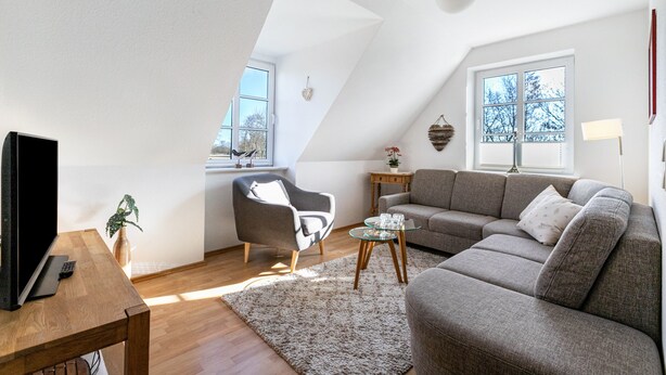 Ein modernes Loft-Apartment mit schrägem Dach, großem Fenster, einer Couch, einem Couchtisch und einem Fernseher auf einem Holztisch.