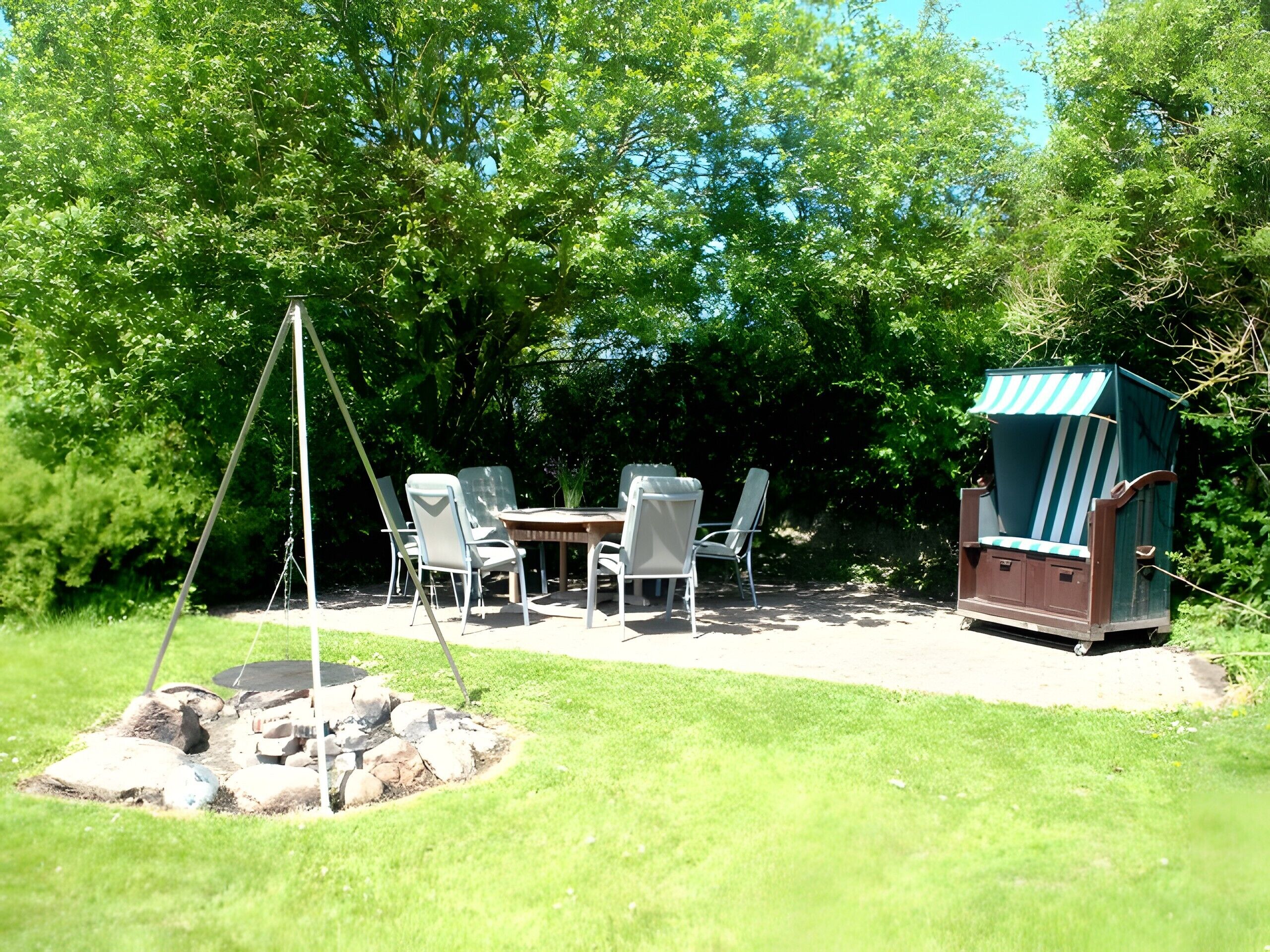 Een terras buiten met een schommel, een tafel en stoelen, omgeven door bomen.
