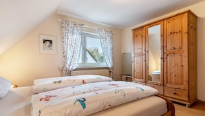 Un dormitorio con dos camas, un armario de madera, un radiador y una ventana con cortinas.
