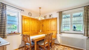 A kitchen with wooden cabinets, a dining table, chairs, a hanging light fixture, and a window with curtains. - Apartment 'Ferienwohnung Talblick' with Mountain View, Shared Terrace and Wi-Fi (Elzach)