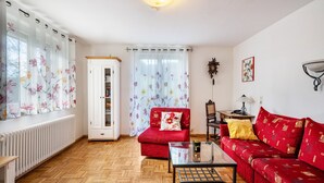 A living room with a red sofa, a glass coffee table, a white cabinet, and a floral curtain. - Apartment 'Ferienwohnung Talblick' with Mountain View, Shared Terrace and Wi-Fi (Elzach)