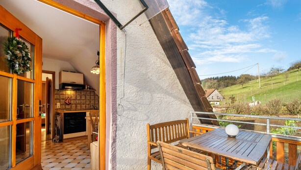 A wooden table and chairs on a balcony with a view of a green landscape. - Apartment 'Ferienwohnung Waldblick' with Mountain View, Shared Terrace and Wi-Fi (Elzach)