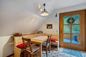 A cozy room with a wooden table and chairs, a bench, a ceiling light, a door with a view, and a small picture on the wall.