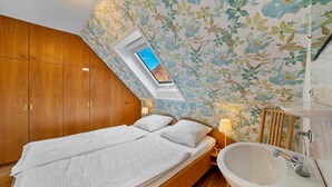 A bedroom with a skylight, wooden wardrobe, a bed, bedside lamps, and a bathroom with a sink. - Apartment 'Ferienwohnung Waldblick' with Mountain View, Shared Terrace and Wi-Fi (Elzach)