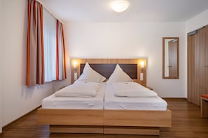 A double bed with wooden headboard and bedside lamps, a mirror, and a wooden floor.