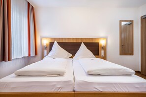 A double bed with white linens, a wooden headboard, bedside lamps, and a mirror on the wall.