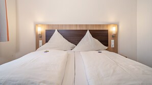 Ein Doppelbett mit Holz Kopfteil, zwei Nachttischlampen und eine schlichte Wand.