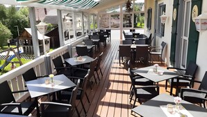 Eine überdachte Terrasse im Freien mit Tischen und Stühlen, ein Holzdeck und Blick auf die Umgebung.