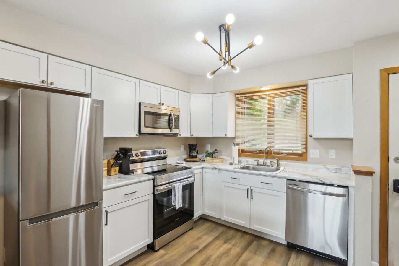 A modern kitchen with stainless steel appliances, white cabinetry, and a wooden floor.