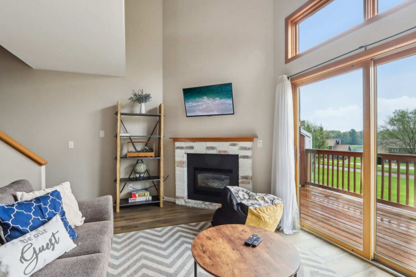 A living room with a fireplace, a sofa, a coffee table, and a balcony with a view of the outdoors.
