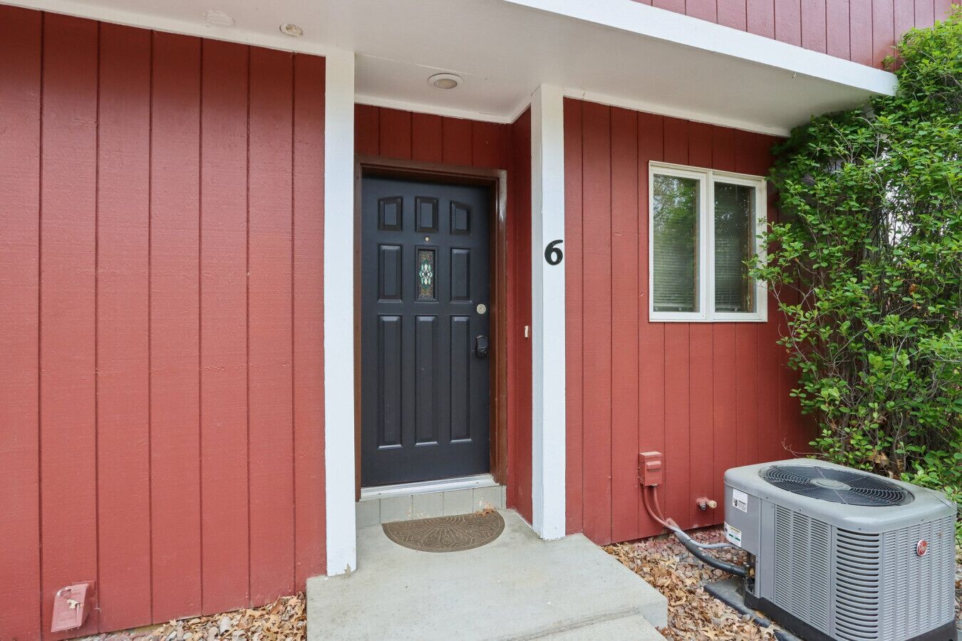 A red building with a black door, a small window, and an air conditioning unit outside.