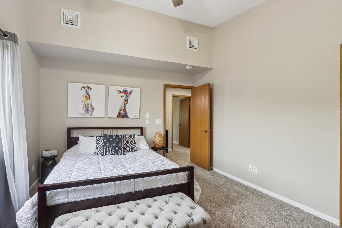 A bedroom with a large bed, a bedside table, a chair, and two wall-mounted artworks.