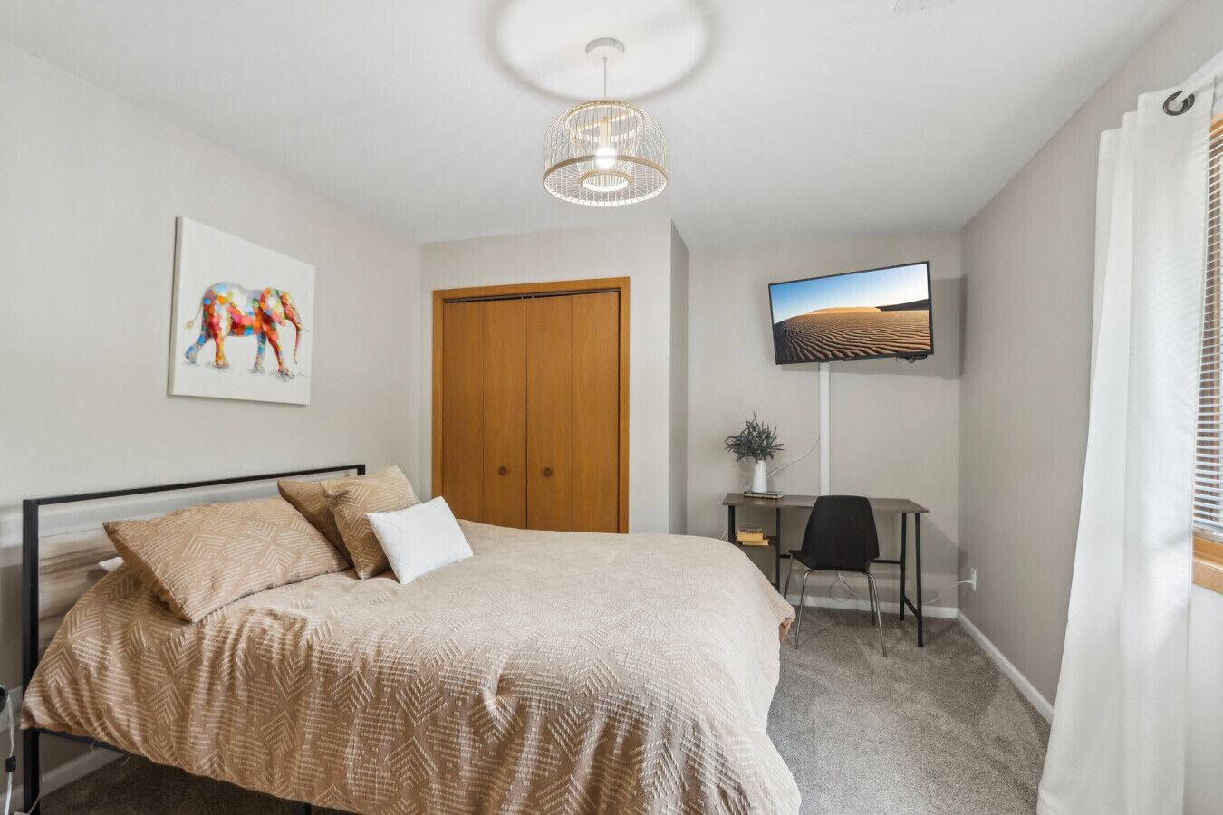 A bedroom with a bed, a desk, a television, and a door.